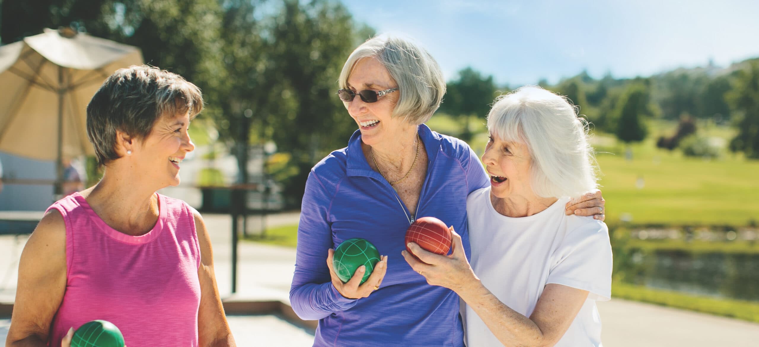 Three women holding Bocce balls laugh and talk.